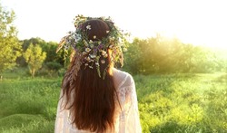 girl in flower wreath on meadow, sunny green natural background. Floral crown, symbol of summer solstice. Slavic ceremony on Midsummer, wiccan Litha sabbat. pagan holiday Ivan Kupala