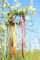 flower wreath with colorful ribbons on tree in Spring garden, natural background. floral decor, Symbol of Beltane, Wiccan Celtic Holiday beginning of summer. pagan witch traditions, rituals