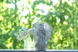 Praying angel and white flowers on table, abstract natural green background. Religious holiday. symbol of faith in God, Christianity church. Easter, Feast of Annunciation to the Blessed Virgin Mary
