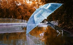 transparent umbrella in water drops in puddle on road, natural abstract blurred background. autumn landscape. symbol of rainy season, bad wet stormy weather. melancholy mood