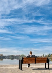 
White clouds in the sky. A young guy sits on a bench by the lake. Feeling Blue. Towards the future. 