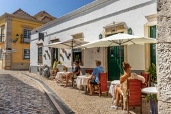 People are sitting at the outside terrace of a small cafe in the historic centre of Faro, Portugal. 