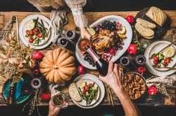 Thanksgiving party table setting. Flat-lay of people pouring champagne and celebrating at table with roasted chicken, vegetables, fig pie, fruit, candles over wooden table background, top view