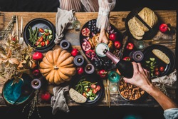 Thanksgiving table setting for family gathering. Flat-lay of man pouring champagne to glass at festive table with roasted chicken, vegetables, fig pie, fruit, candles over wooden background, top view