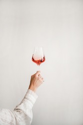 Womans hand in white shirt holding glass of rose wine over white wall background. Wine shop, wine tasting, bar, wine list concept