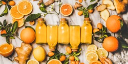 Immune boosting vitamin health defending drink. Flat-lay of fresh turmeric, ginger, citrus juice shot in glass bottles over marble background, top view. Pure vegan Immunity system booster