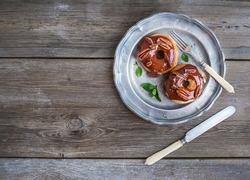 Cinnamon donuts with caramel icing and pekans served with fresh mint and cane sugar on a vintage metal plate over a white table cloth over a rustic wood background with a copy space. Top view