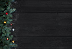 Christmas or New Year decoration background: fur-tree branches, colorful glass balls on black wood background with copy space