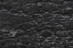 Dark black old medieval natural stone wall. Texture, background or wallpaper