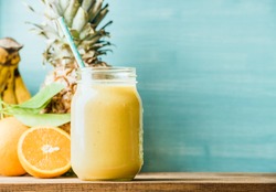 Freshly blended yellow and orange fruit smoothie in glass jar with straw. Turquoise blue background, copy space