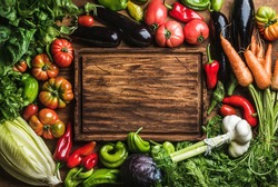 Fresh raw vegetable ingredients for healthy cooking or salad making with rustic wood board in center, top view, copy space. Diet or vegetarian food concept, horizontal composition