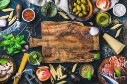 Italian food cooking ingredients on dark background with rustic wooden chopping board in center, top view, copy space