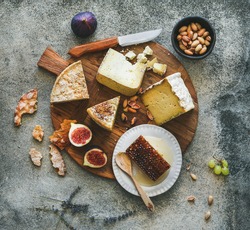 Flat-lay of cheese platter with cheese assortment, figs, honey and nuts over grey concrete background, top view. Party or gathering eating concept