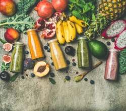 Flat-lay of colorful smoothies in bottles with fresh tropical fruit and vegetables on concrete background, top view, copy space. Healthy, vegetarian, detox, dieting breakfast food concept