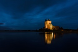 Old Irish Dunguaire Castle by the water at night with reflection