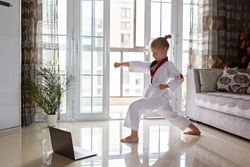 Taekwondo girl in kimono with white belt exercising at home in living room. Online education during coronavirus covid-19 lockdown, self isolation and social distancing concept