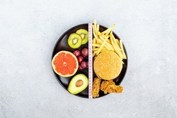 Flat lay of Healthy and unhealthy food from fruits and vegetables vs fast food, sweets and pastry in black plate on gray concrete background. Diet and detox against calorie and overweight lifestyle
