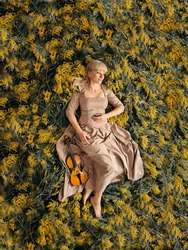 Girl with a violin in mimosa. Spring melody. Music and holiday concept. The awakening of nature.