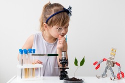 Little girl is behind the desk. Microscope and the tree are near her. Little robot. E-learning. Stem education.