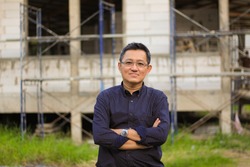 half body portrait of an asian man in crossed arms position with construction site as a background