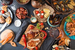 Overhead of dinner table. Barbecue meat and seafood with vegetable. Pork grilled steaks, grilled salmon trout, mussels, shrimps, dried tomato, cherry tomato,  glass of  wine. Picnic bbq party concept.