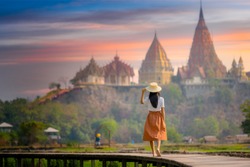 young farmer woman walks on wooden bridge terrace of rice to the temple at morning sunrise with scenerry view of buddhist temple pagoda in background