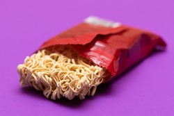 Opened Package with Uncooked Instant Noodles on Violet Background. Raw Pasta. Dry Asian Fast Food. Quick Lunch