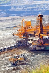 Bucket wheel excavator and bulldozer at work in coal mine. Mining industry from above. Open pit in Central Europe. Heavy industry before Green deal.