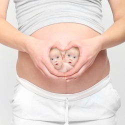 Love and new life. A woman's hands forming a heart symbol with twins on her belly. 