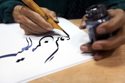 man hands writing arabic calligraphy with ink