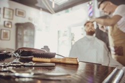 Accesories for cutting on the table in a barbershop and a hairdresser works in the background.  Photo in vintage style
