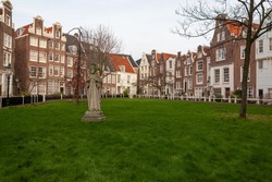 Begijnhof  is one of the oldest inner courts of Amsterdam with group of historic buildings and Jesus statue with green lawn in foreground, Netherlands. 