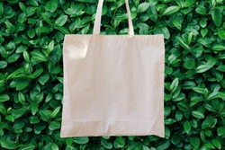 Blank White Mockup Linen Cotton Tote Bag on Green Bush Trees Foliage Background. Eco Nature Friendly Style. Environmental Conservation Recycling Concept. Template for Artwork Text. Japanese