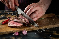 Cooking juicy beef steak by chef hands on dark black background with copy space for text menu or recipe.