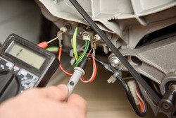 Washing machine fix. Man's hands measure the resistance of a heating element with a multimeter