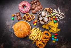 Junk food concept. Unhealthy food background. Fast food and sugar. Burger, sweets, chips, chocolate, donuts, soda on a dark background.
