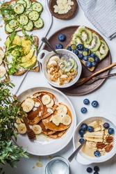 Healthy varied vegetarian breakfast table. Oatmeal with fruits, chia pudding, pancakes with banana and honey and toasts with fruits, vegetables and cream cheese, white background.