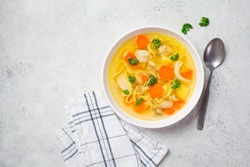 Homemade chicken soup with noodles and vegetables in a white bowl, white background. Healthy warm comfortable food.