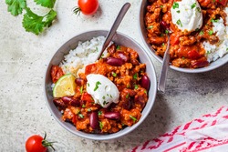 Chili con carne with rice in a gray bowl. Beef stew with beans in tomato sauce with sour cream and rice. Traditional Mexican food concept.