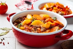 Beef stew with potatoes and carrots in tomato sauce in red pot, gray  background. Slow cooking concept.