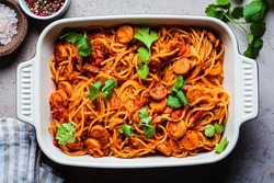 Baked spaghetti pasta with sausages in tomato sauce in the oven dish, top view.