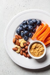 Vegan healthy snacks plate - carrots, nuts, berries and peanut butter, top view.