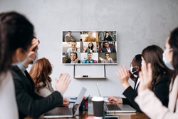 Business meeting.A group of formal successful people wearing protective masks sit at the table and communicate online via videoconference with colleagues discussing about important business strategies
