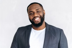 Close-up portrait of an attractive African American male entrepreneur, freelancer or student in stylish suit, standing in the office, looking and smiling friendly at the camera