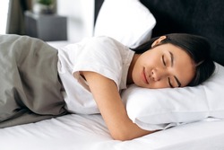 Sweet dreams. Pretty chinese woman in white t-shirt under the blanket in bed in the morning. Side view of a sleeping asian girl in a cozy bed in apartment, pleasant dreams, healthy sleep