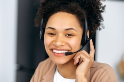 Close-up of successful pleasant african american girl, with headset, expert, consultant or call center operator, looks at camera, smile friendly. Support service concept, hotline, distant consultation