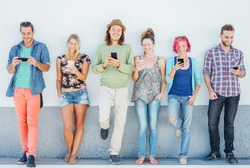 Young people watching on their smart mobile phones leaning on a wall - Generation addicted to new technology - Concept of youth addiction to social network trends 