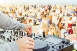 Close up of DJ's hand playing music at turntable at beach party festival - Crowd people dancing and having fun in club outdoor - Concept of youth summer party lifestyle