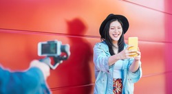 Asian fashion woman vlogging and using mobile smart phone outdoor - Happy Chinese trendy girl having fun making video with gimbal camera - Millennial people, Generation z and technology concept 