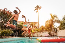 Group happy friends jumping in pool at sunset time - Crazy young people having fun making party in exclusive tropical house - Summer holidays vacation and youth culture lifestyle concept
